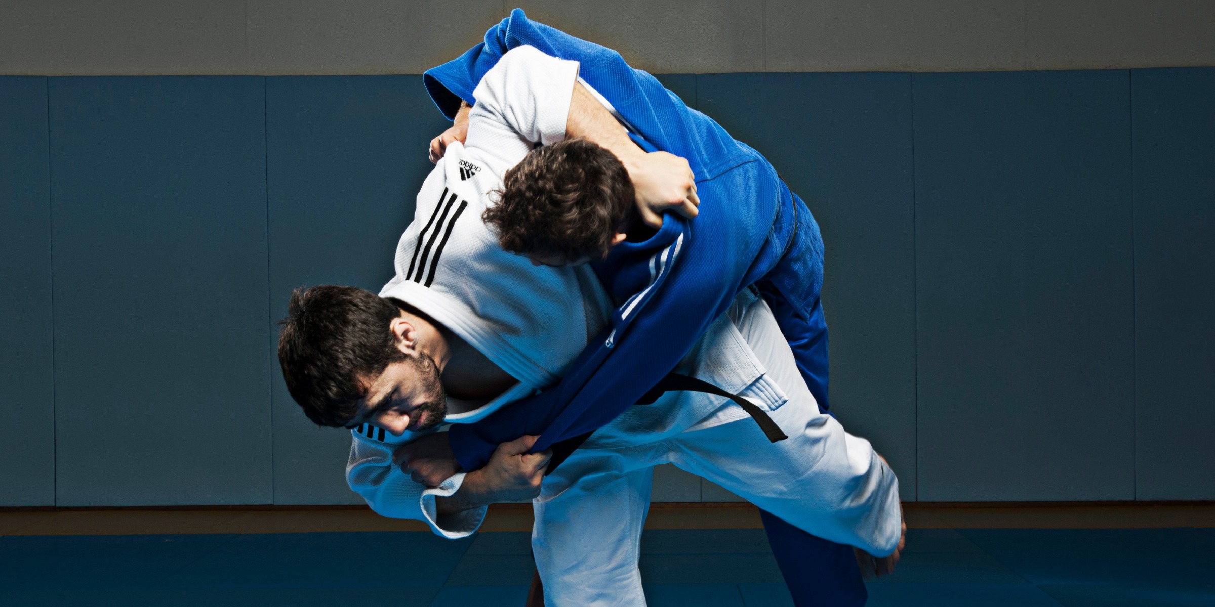 Two judoka in white and blue adidas judo uniforms mid-throw